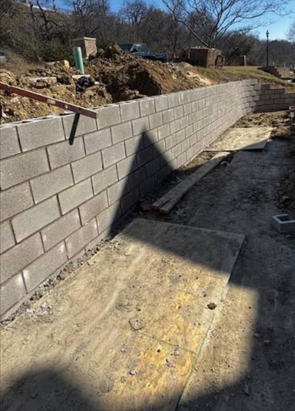 Construction site with a long gray retaining wall beside a dirt path and excavated slope.