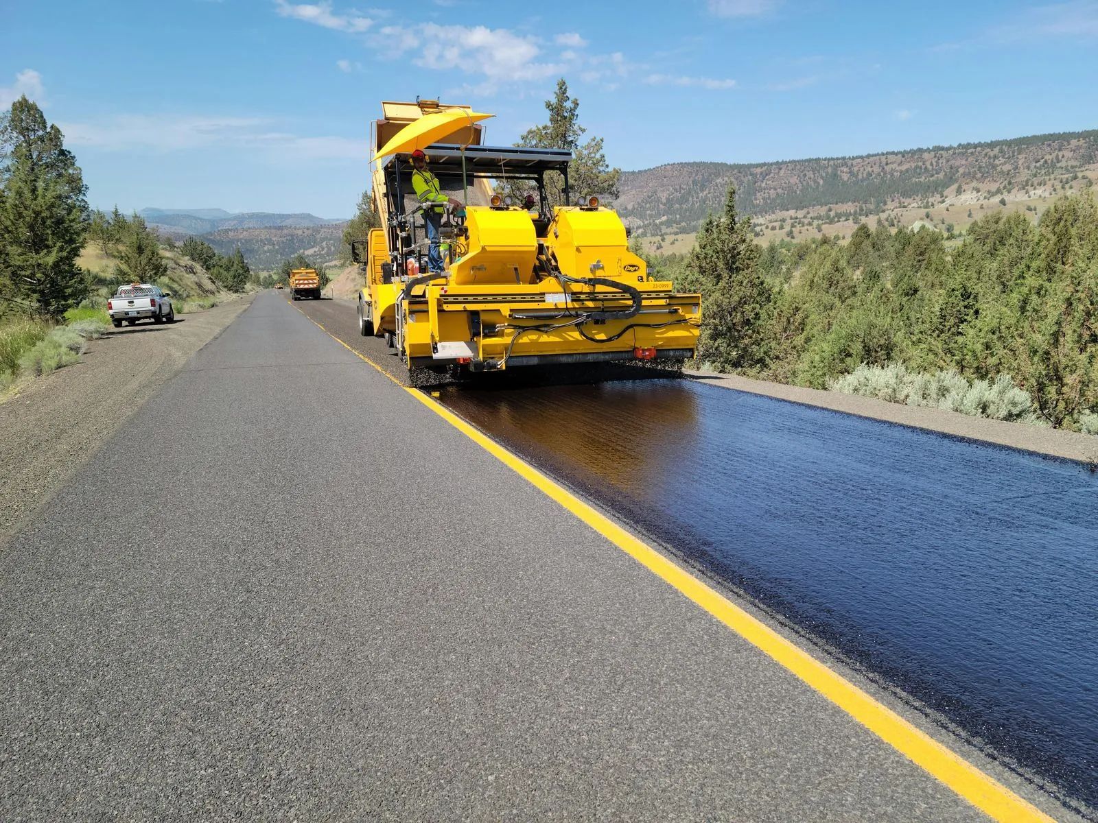 Yellow road paving machine laying fresh black asphalt on a rural highway lane