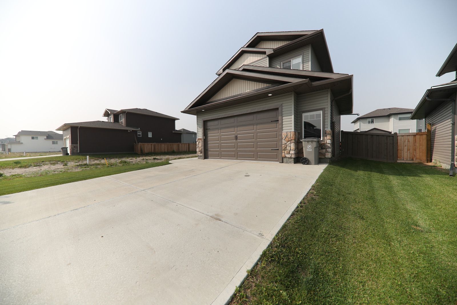 Suburban house with a two-car garage, concrete driveway, and green lawn under a clear sky
