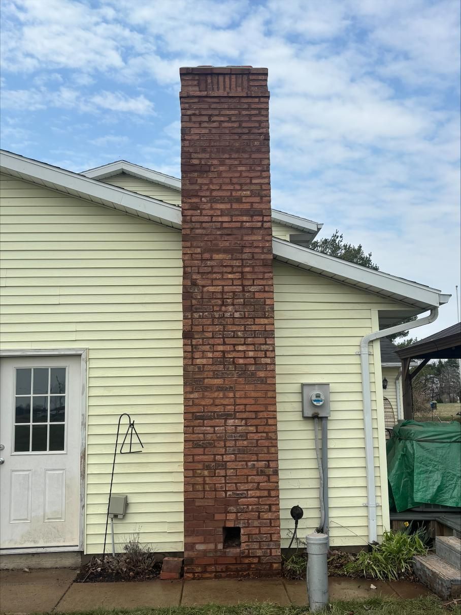 Brick chimney on the exterior of a pale yellow house, beside a white door and utility meter.