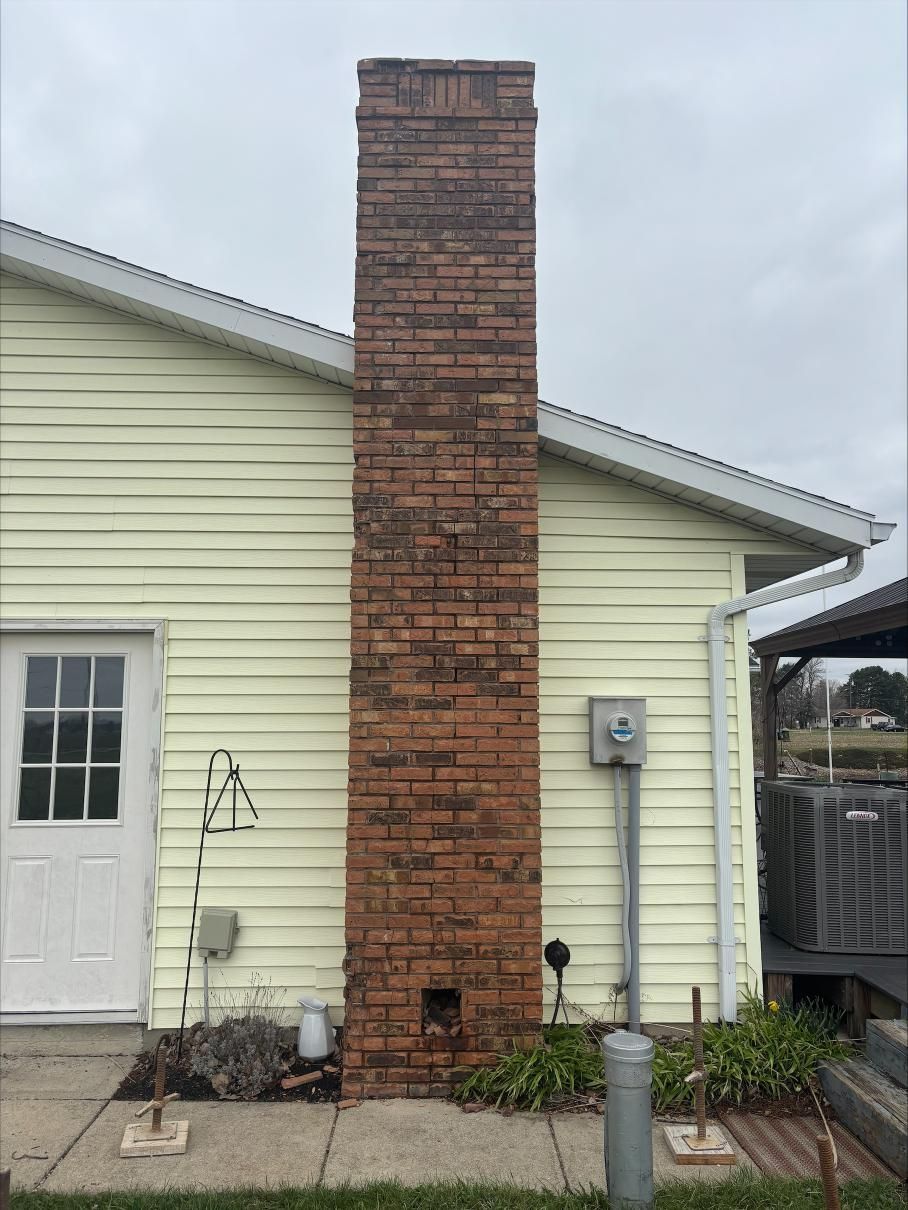 Red brick chimney on the side of a pale yellow house with a white door and overcast sky