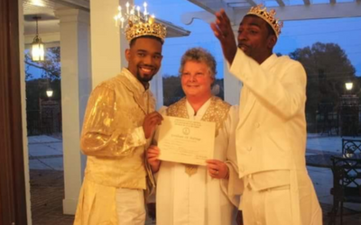 Three people in gold crowns pose with a certificate indoors at sunset.