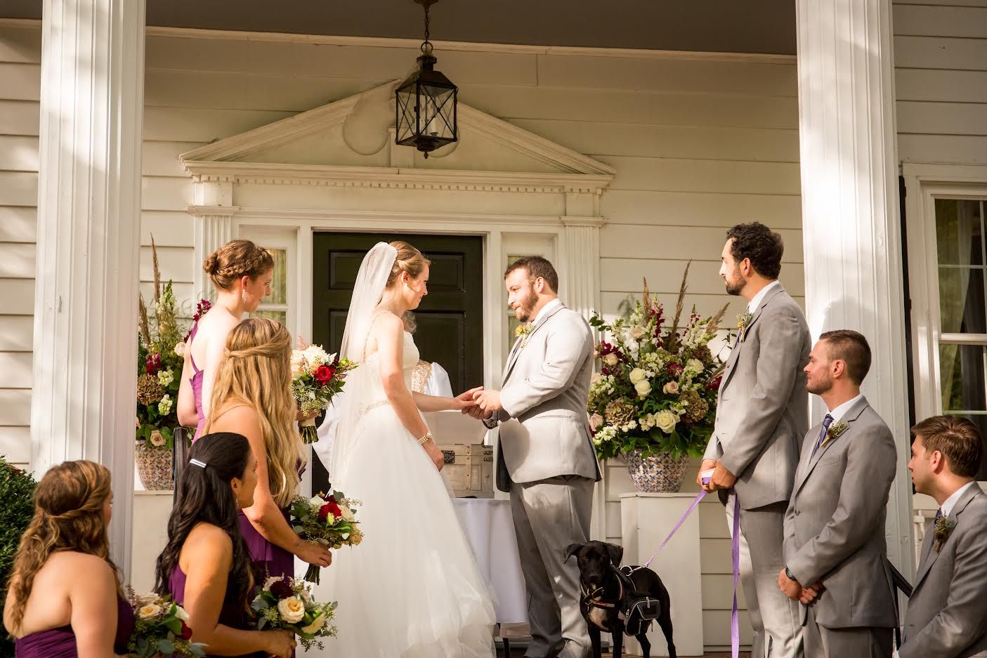 Wedding ceremony on a porch, bride and groom exchanging vows with attendants and guests nearby.