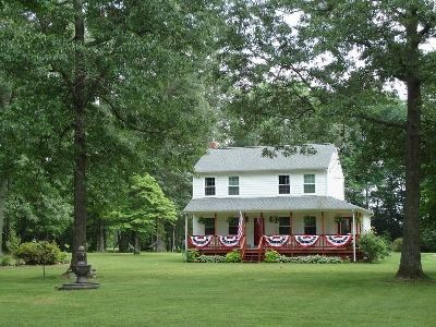 White house with a porch decorated in red-white-blue bunting, set in a grassy yard with large trees.