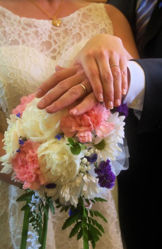 Hands with wedding rings holding a white and pink bridal bouquet