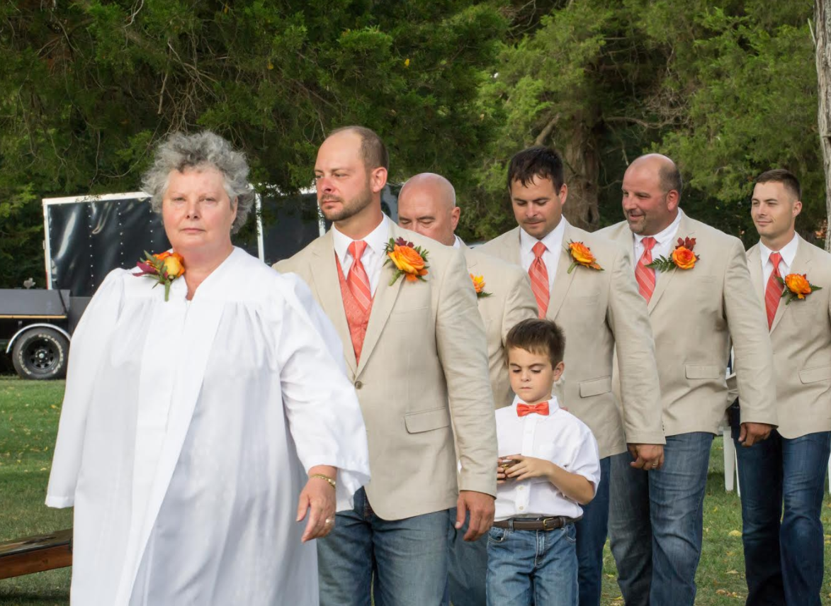 People in matching beige jackets and orange ties walking outdoors, with a child in front.