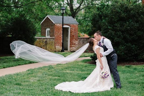 Bride and groom kissing in a garden, with the bride’s veil blowing in the wind.