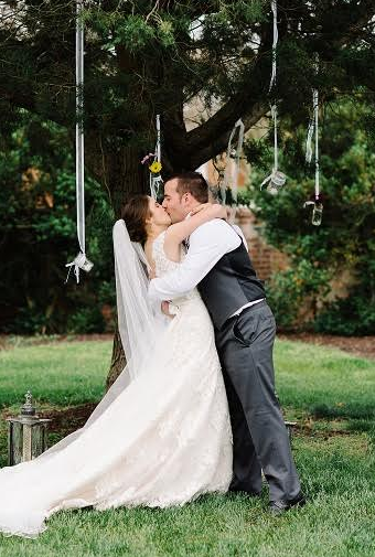 Bride and groom kissing under a tree in a garden, with the bride’s veil flowing over the grass.