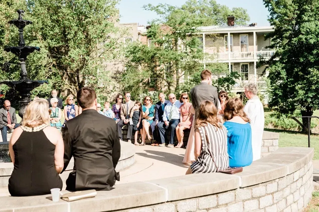 People seated and standing around an outdoor stone amphitheater during a ceremony in a park