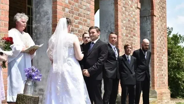 Wedding couple exchanging vows outdoors at a brick church entrance, with guests nearby.