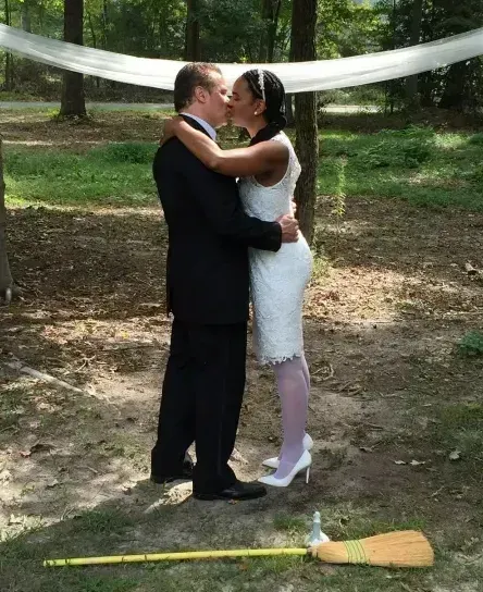 Couple in formalwear embracing outdoors beneath a white draped fabric canopy.