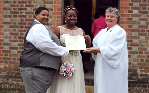 Three people holding a certificate in front of a brick wall, with one person holding a bouquet
