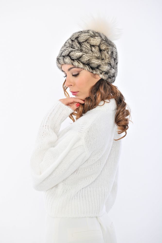 Donna che indossa un cappello fantasia e un maglione bianco, guarda in basso con un'espressione contemplativa.