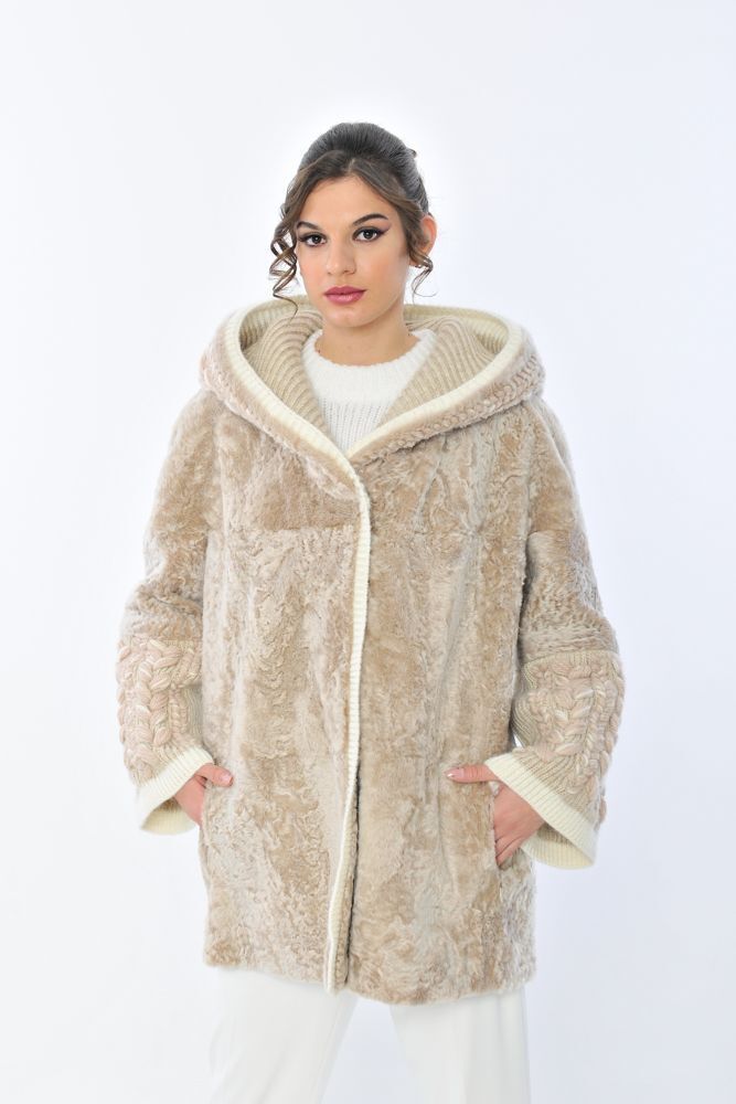 Donna in piedi con le mani in tasca e un cappotto marrone chiaro con cappuccio e rifiniture bianche.