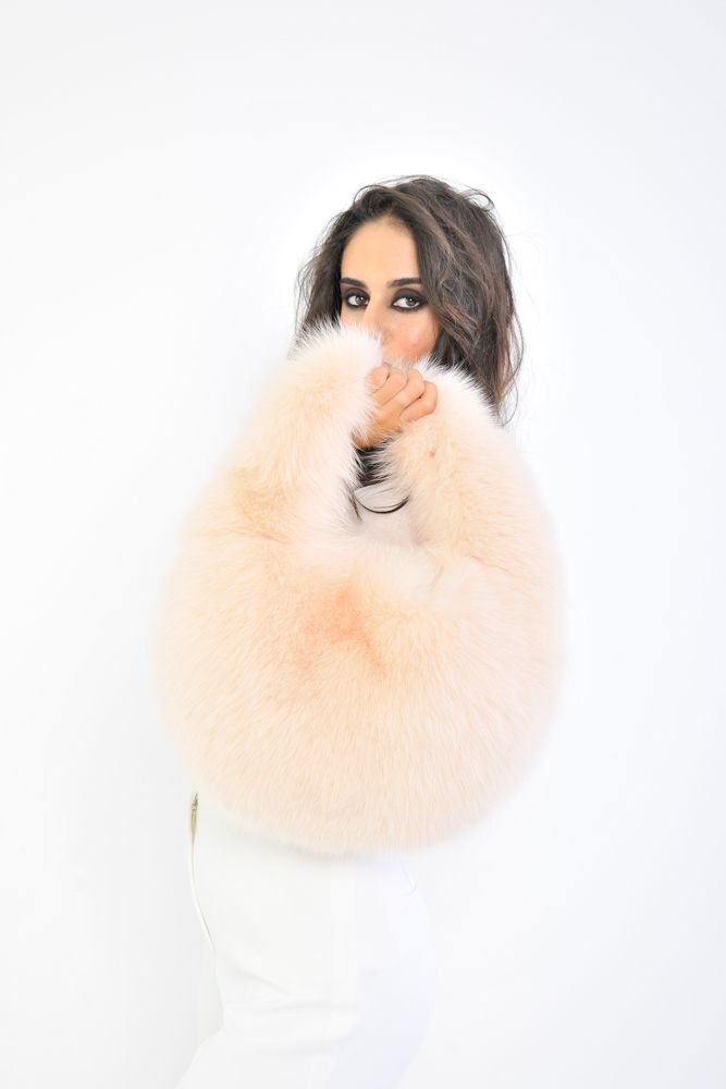 Una donna tiene davanti al viso un soffice accessorio di pelliccia color pesca, su uno sfondo bianco.