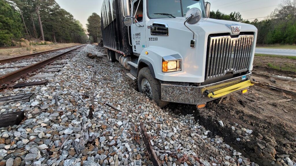 A white semi truck is driving down train tracks.