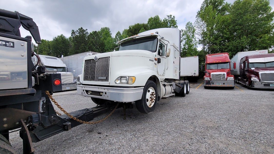 A semi truck is being towed by a trailer in a parking lot.