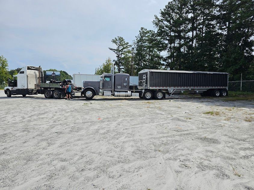 Two semi trucks are parked in a dirt lot with trees in the background. Two semi trucks are parked in a dirt lot with trees in the background.