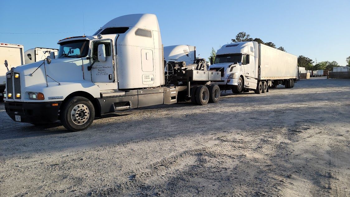 A white semi truck is being towed down a road by a tow truck.