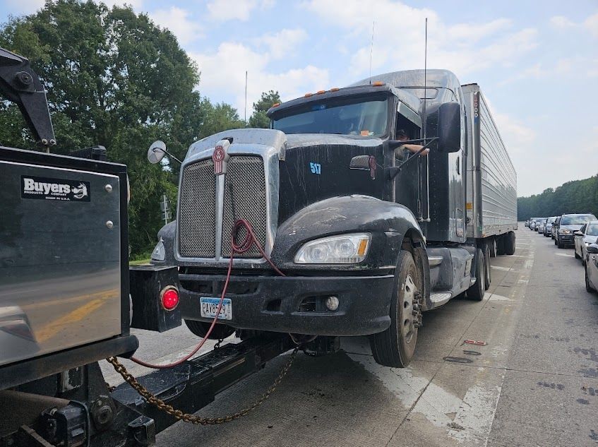 A black semi truck is being towed by a tow truck on a highway. A black semi truck is being towed by a tow truck on a highway.