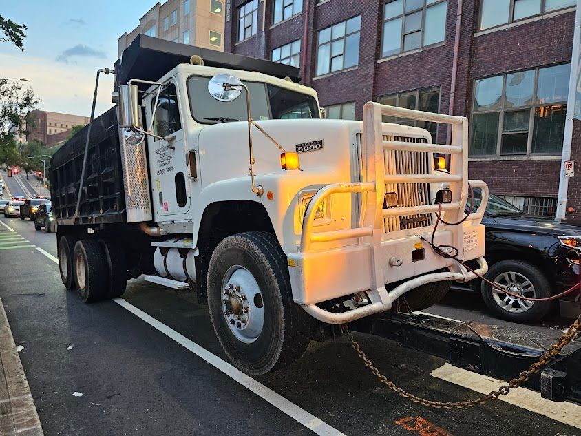A white and black dump truck is parked on the side of the road. A white and black dump truck is parked on the side of the road.
