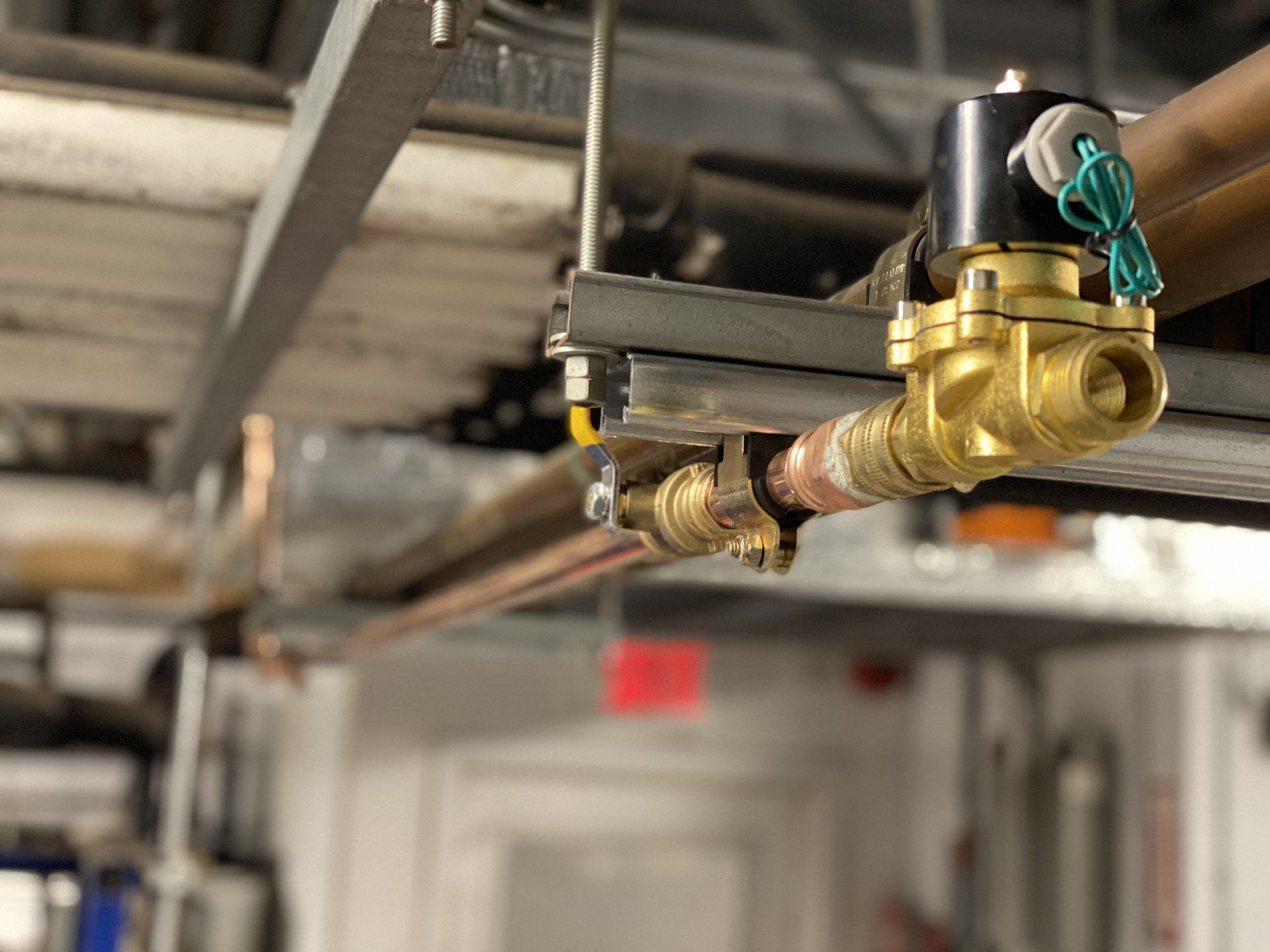 Copper pipes with a brass solenoid valve attached to a ceiling framework in a building.