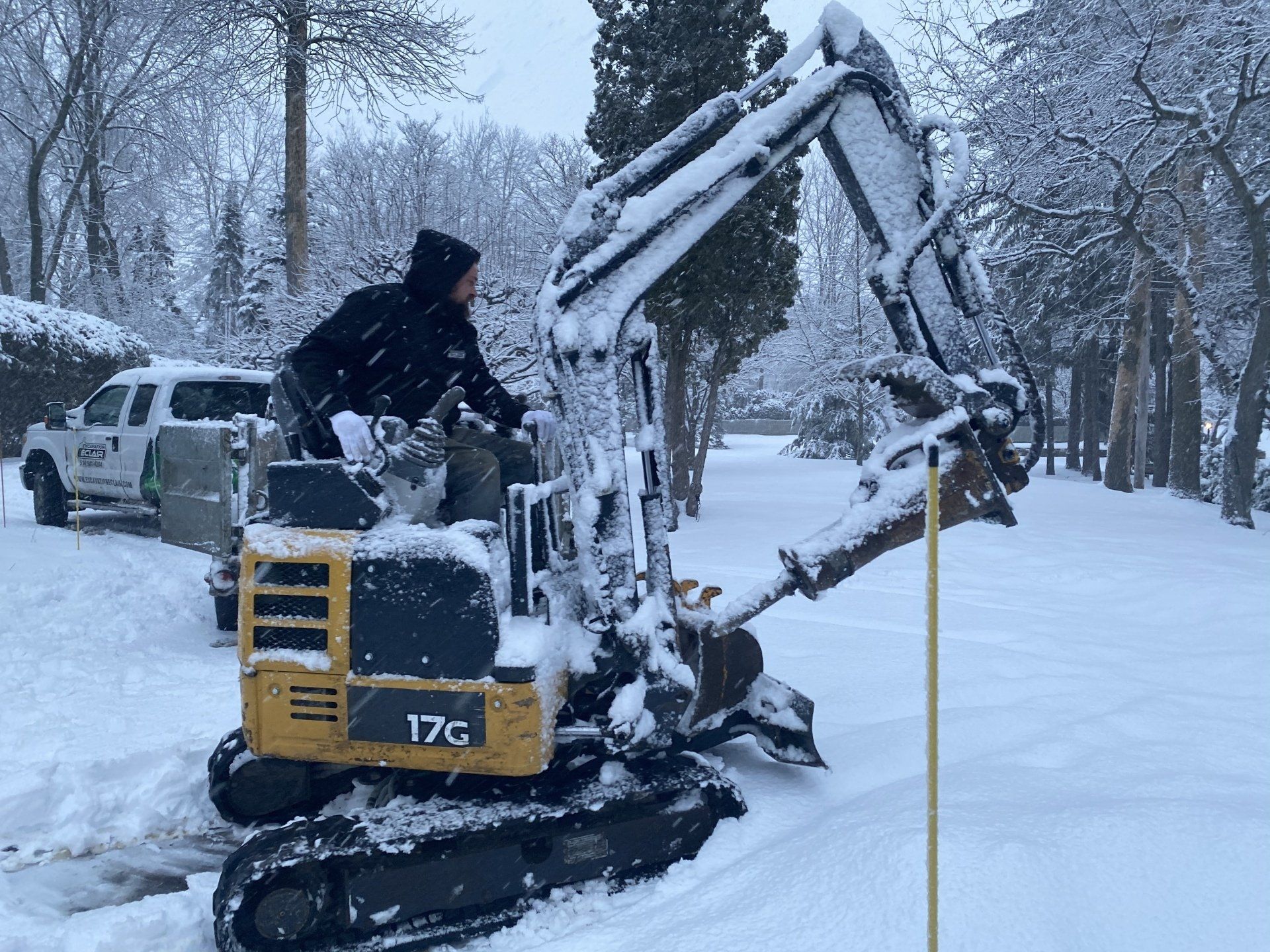 Une pelleteuse enneigée, conduite par une personne, déblaye la neige. Paysage résidentiel enneigé.
