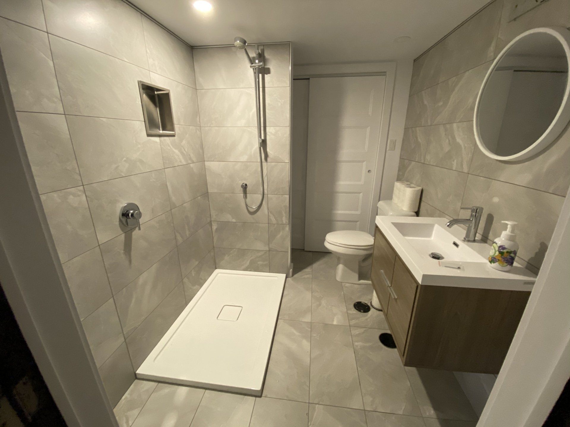 Bathroom with a walk-in shower, vanity, and toilet; gray tile walls and floor.