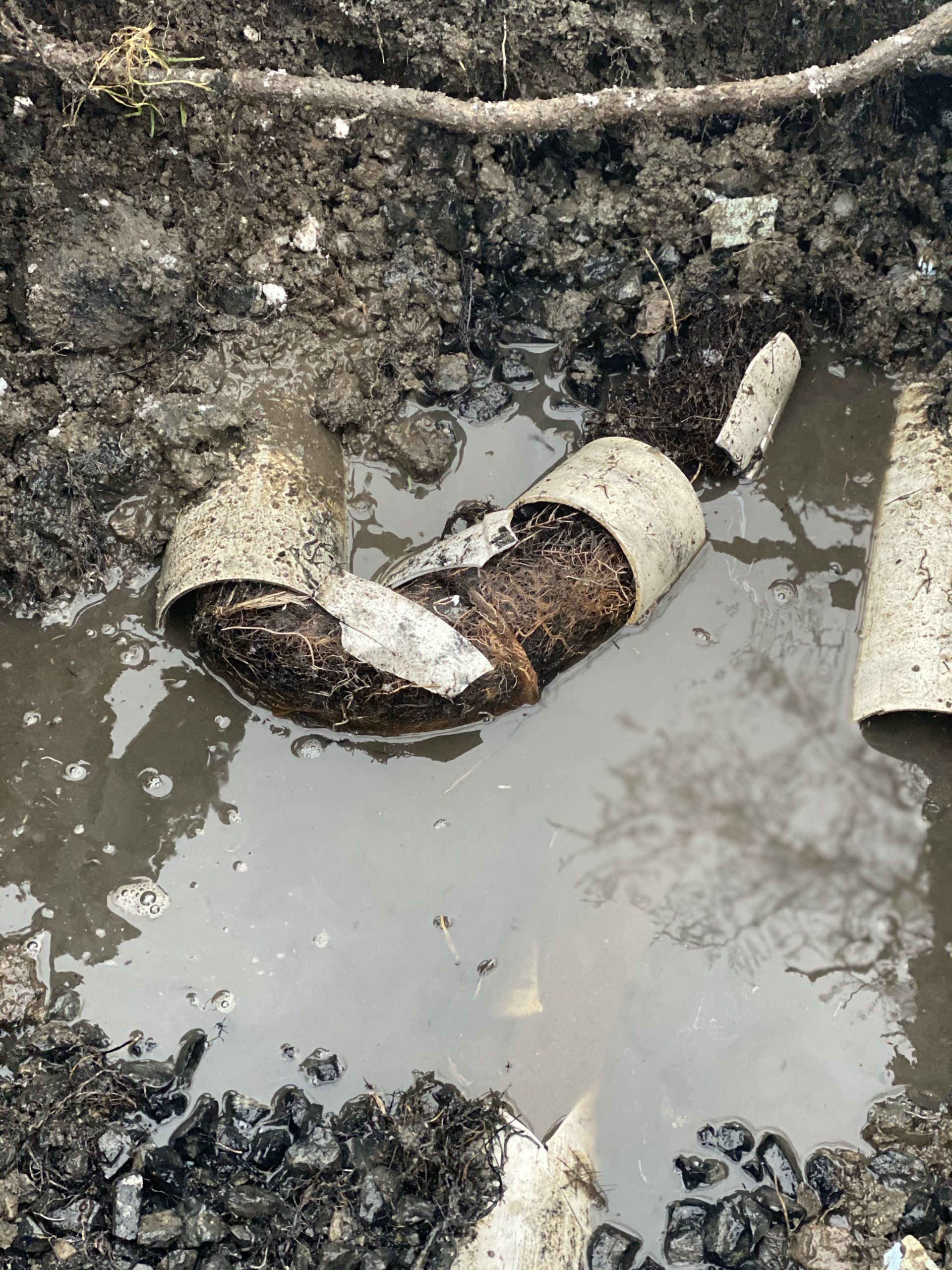 Coude de tuyau cassé dans un sol boueux, entouré d'eau et de terre sombre.