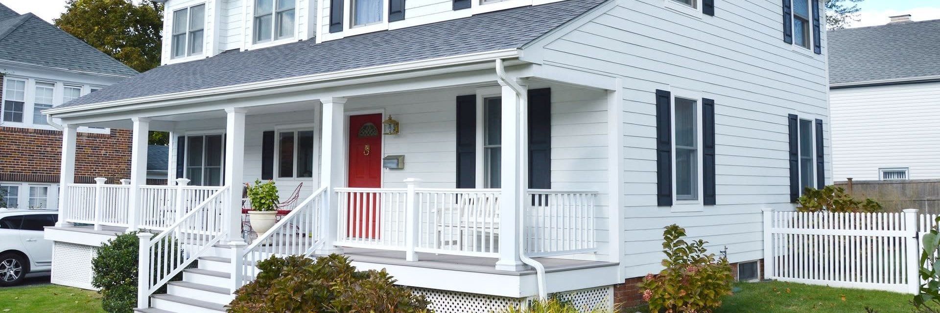 White house with a red front door and a wraparound porch.