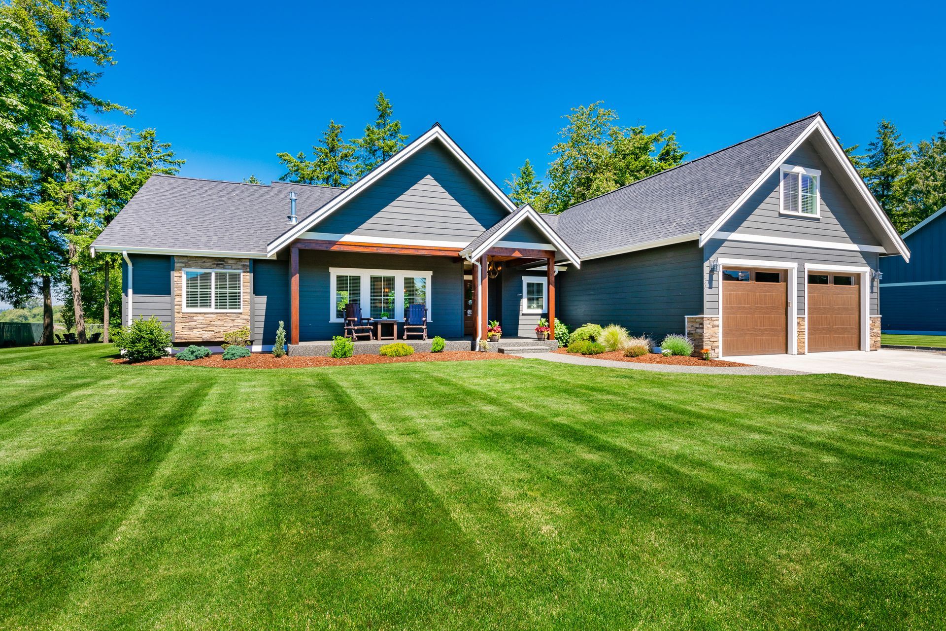 Blue house with attached garage, lush green lawn, bright blue sky.