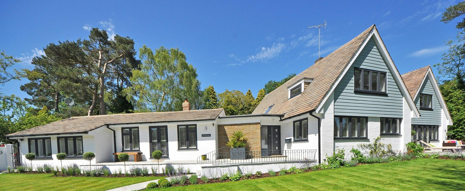 White house with black windows under a blue sky. Green grass, trees, and stone porch.