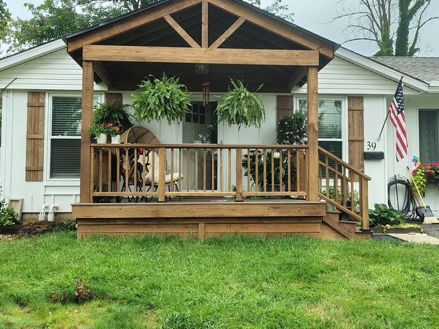 Cottage home with a wooden porch, hanging plants, and an American flag.