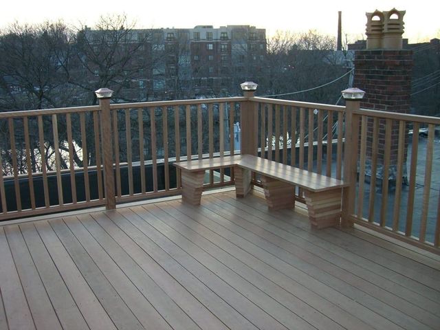 Wooden deck with built-in bench and railing. City buildings visible in the background.