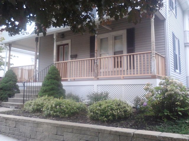 Gray house with a porch, wooden railing, and landscaping. Steps lead to the front door.
