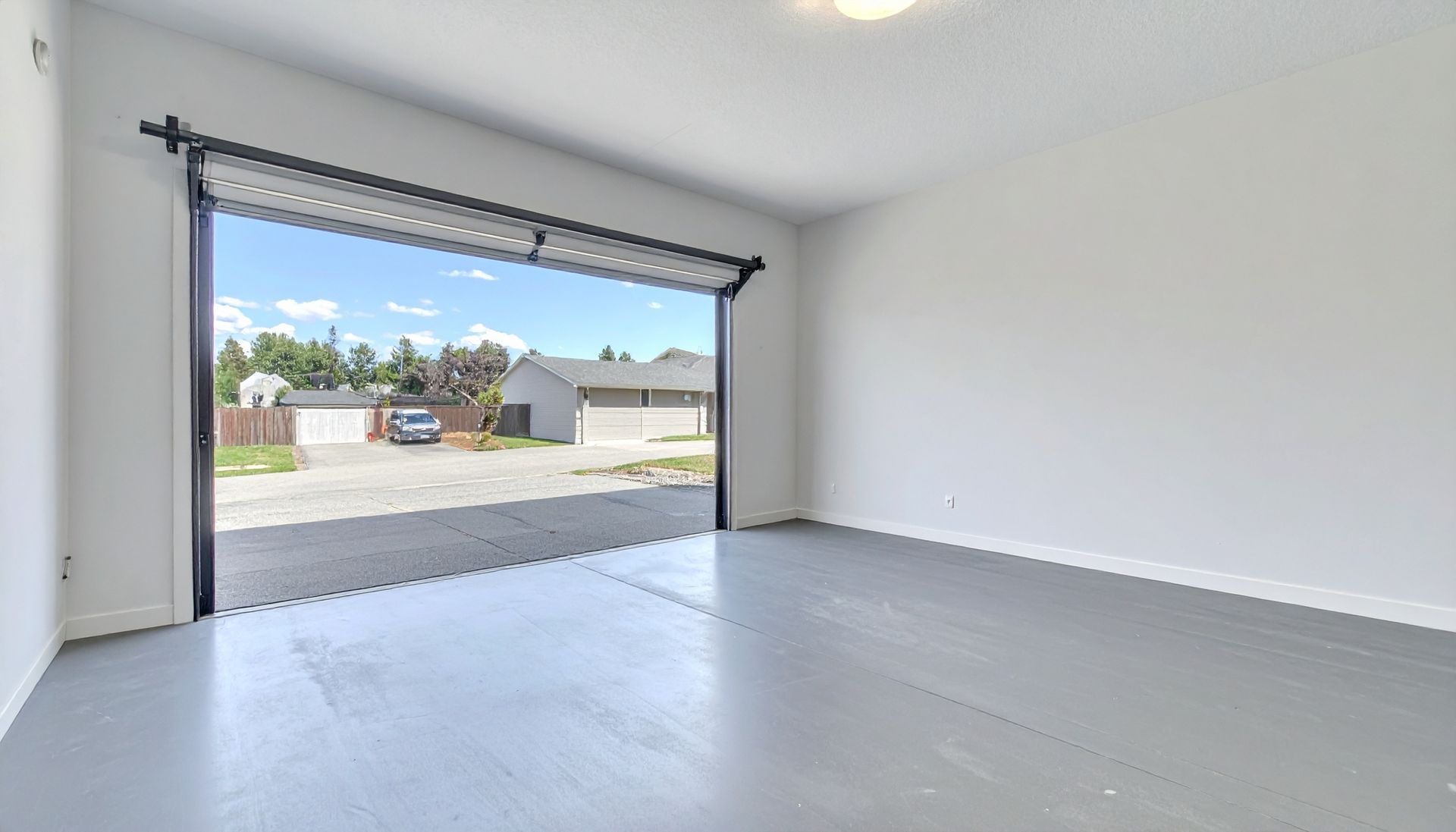 Empty garage with open door, showing the outside street view. Gray floor, white walls.