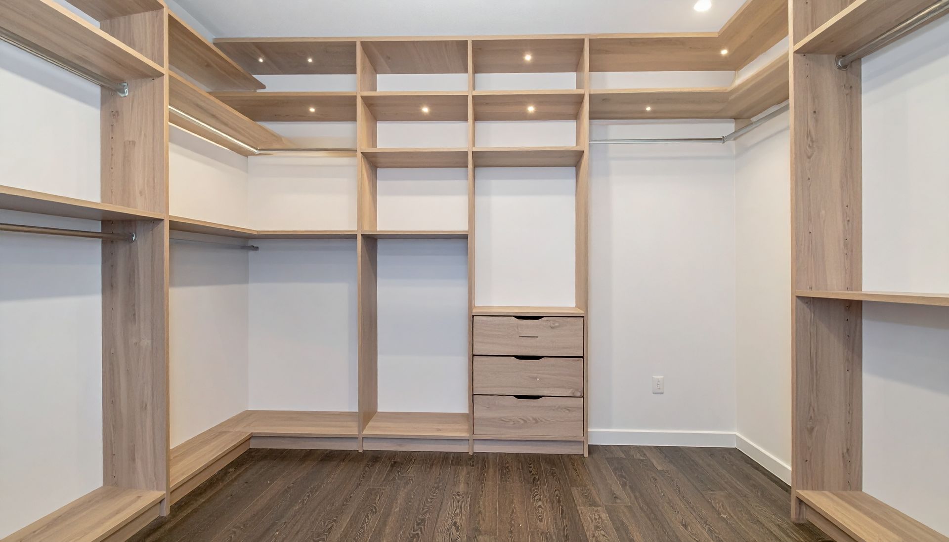 Walk-in closet with light wood shelving, drawers, and rod; dark wood floor, white walls.