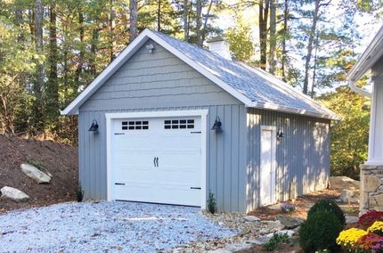 Blue-sided garage with white door and roof. Gravel driveway, surrounded by trees.