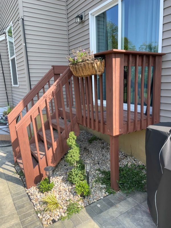 Brown wooden deck stairs with a small garden and a hanging basket, next to a house with a sliding glass door.