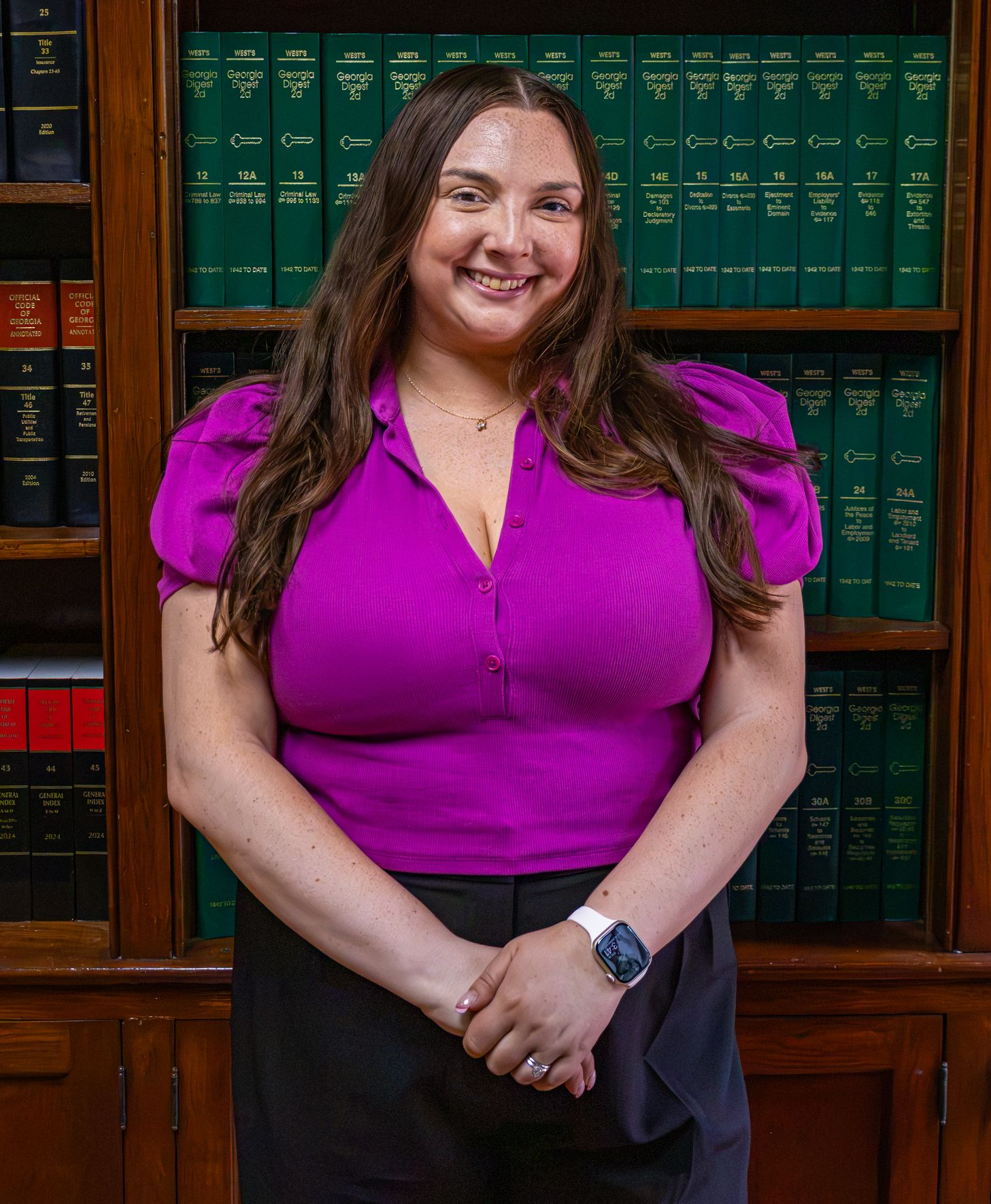 Woman in a magenta blouse standing in front of a bookshelf of green legal volumes