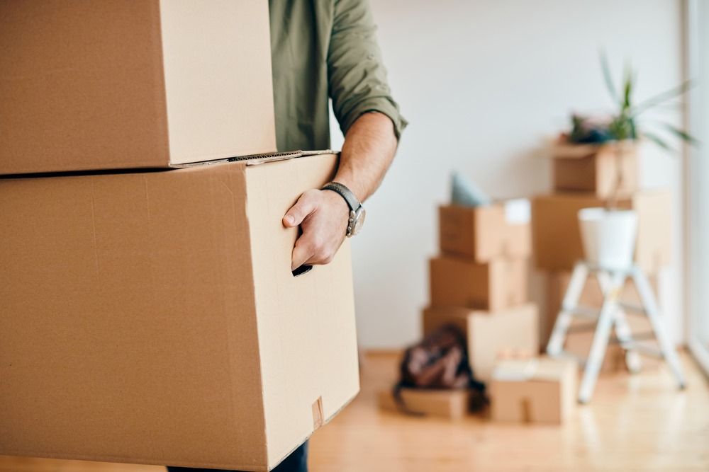 A Man is Carrying a Stack of Cardboard Boxes in a Room — North Coast Storage in North Boambee Valley, NSW