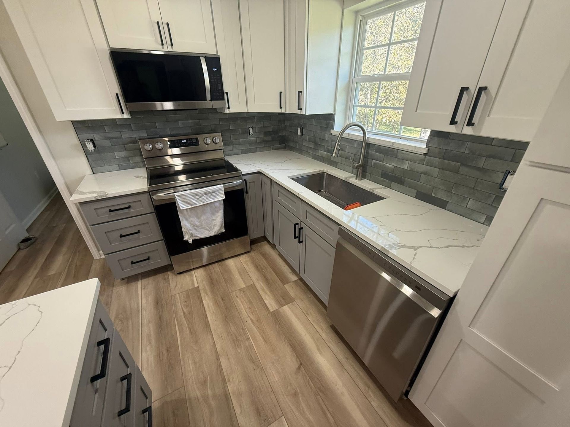Bright modern kitchen with white cabinets, stainless steel appliances, and a window over the sink