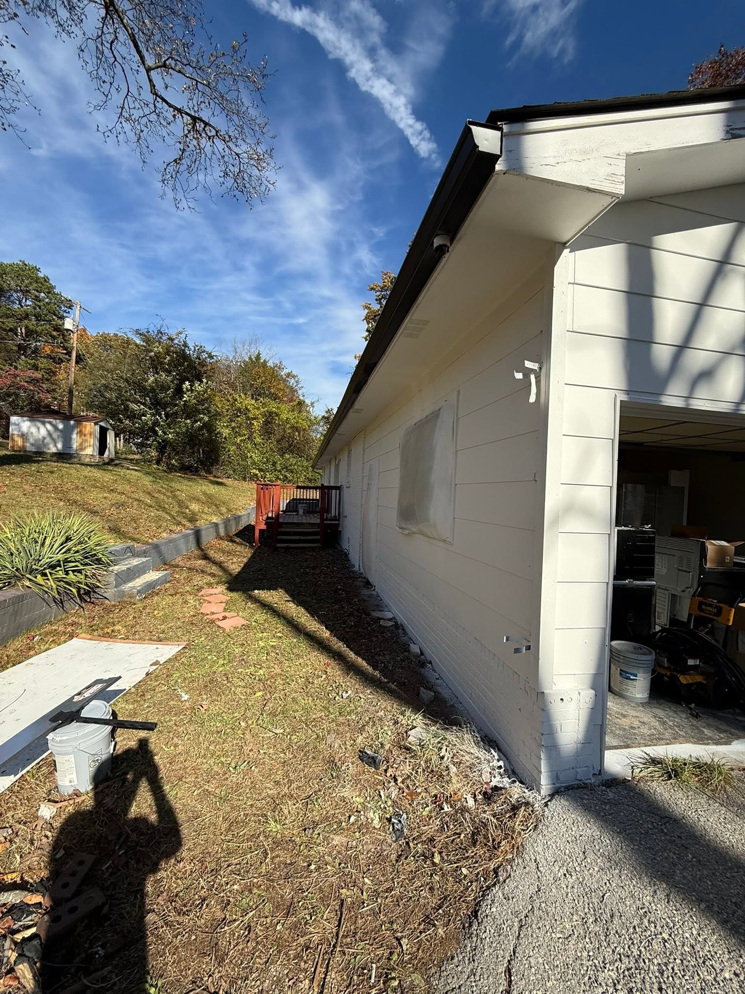 Backyard beside a white house with a gravel path, trees, and blue sky.