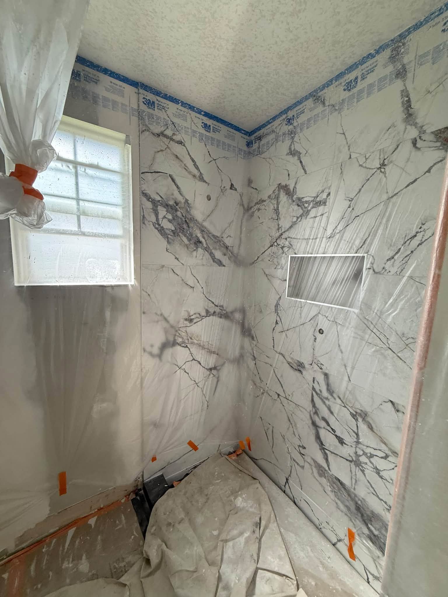 Small bathroom shower under renovation with marble-look wall panels and a covered floor.