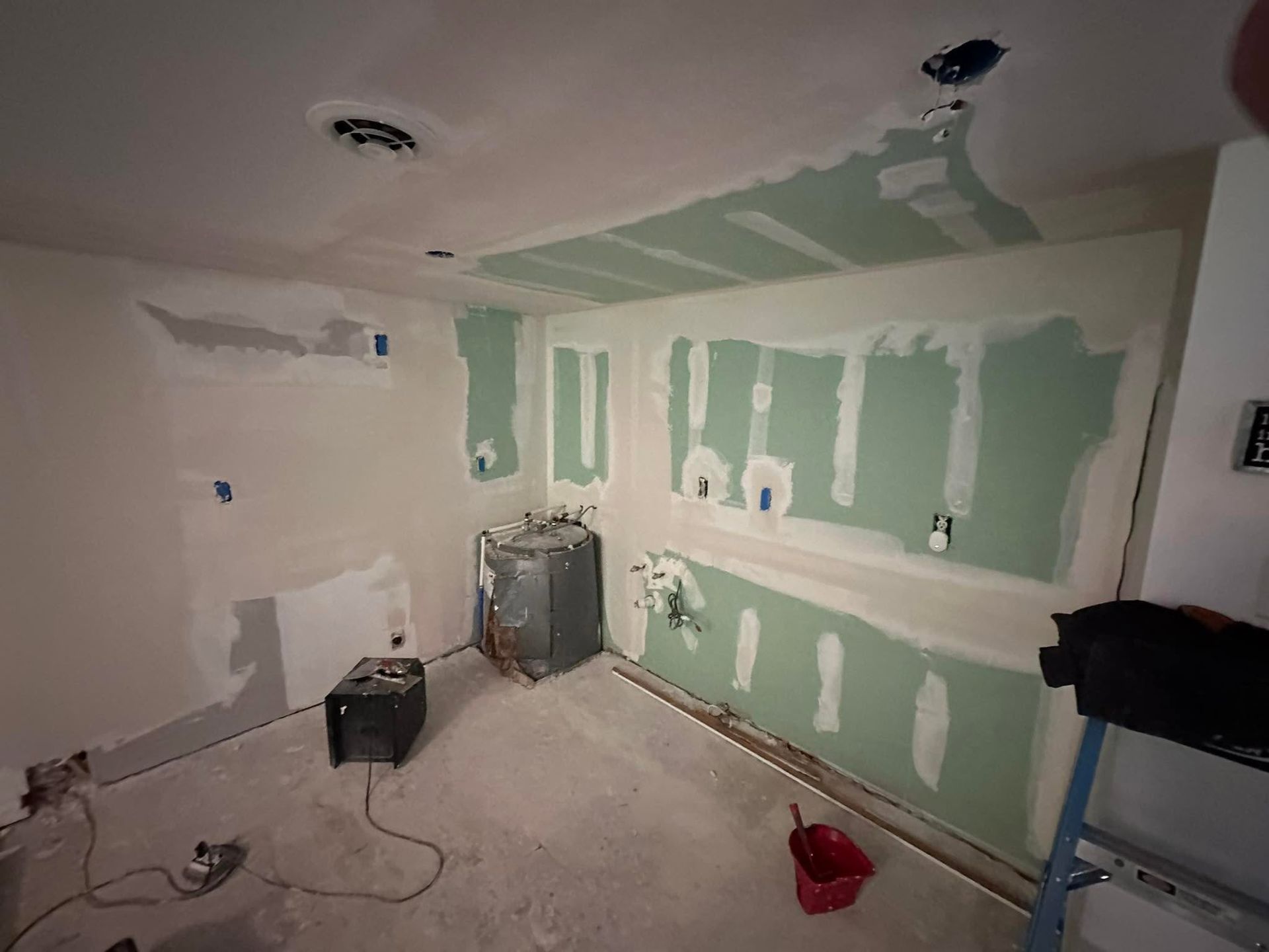 Partially renovated room with green drywall patches, tools, and paint supplies on the floor