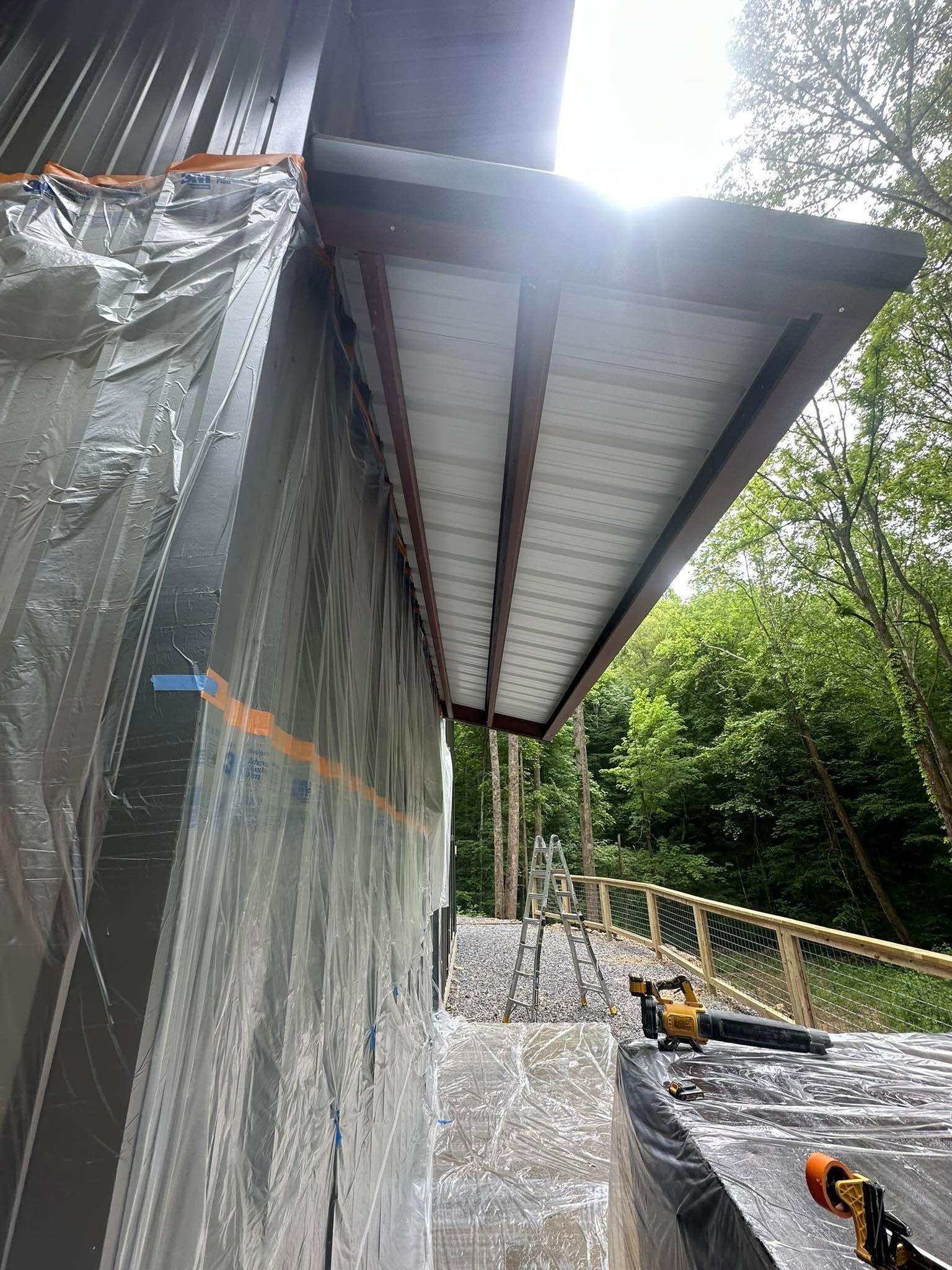Metal roof over a partially enclosed structure with construction materials and trees in the background