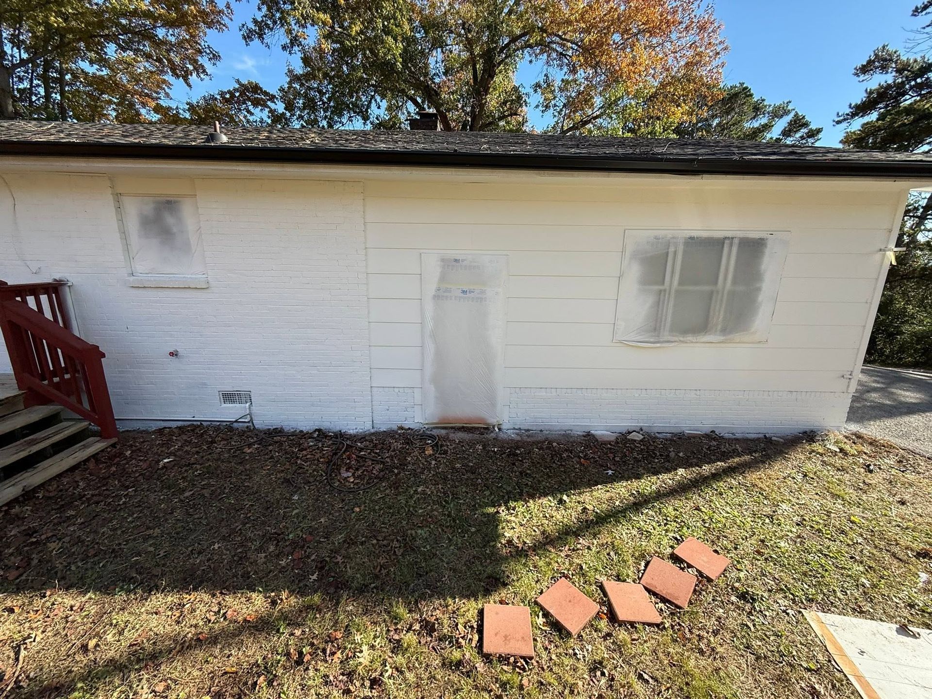 White shed with door and windows in a yard, autumn trees above, red stairs on the left.