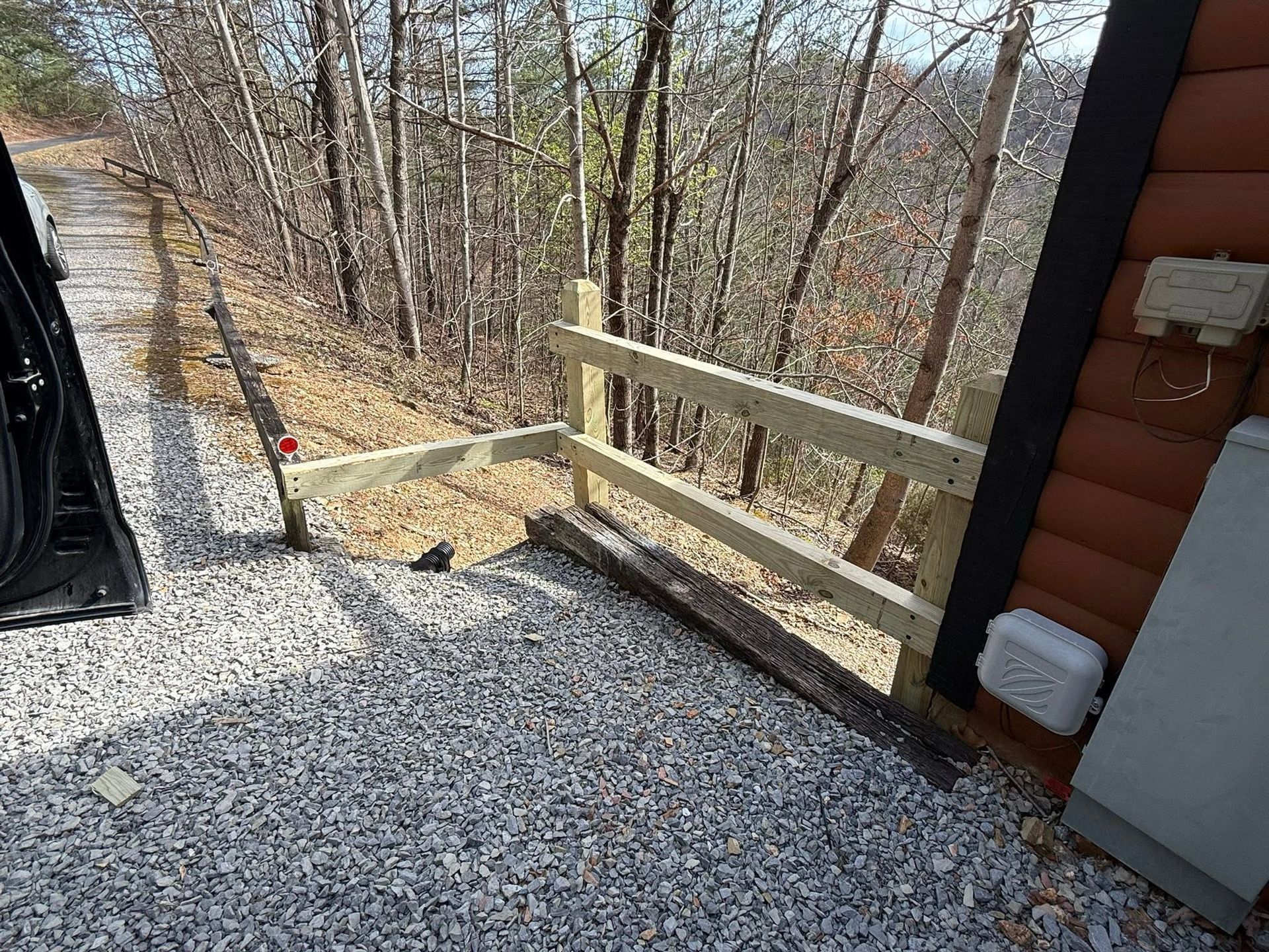 Gravel path beside a log cabin, with a wooden railing and wooded hillside beyond.
