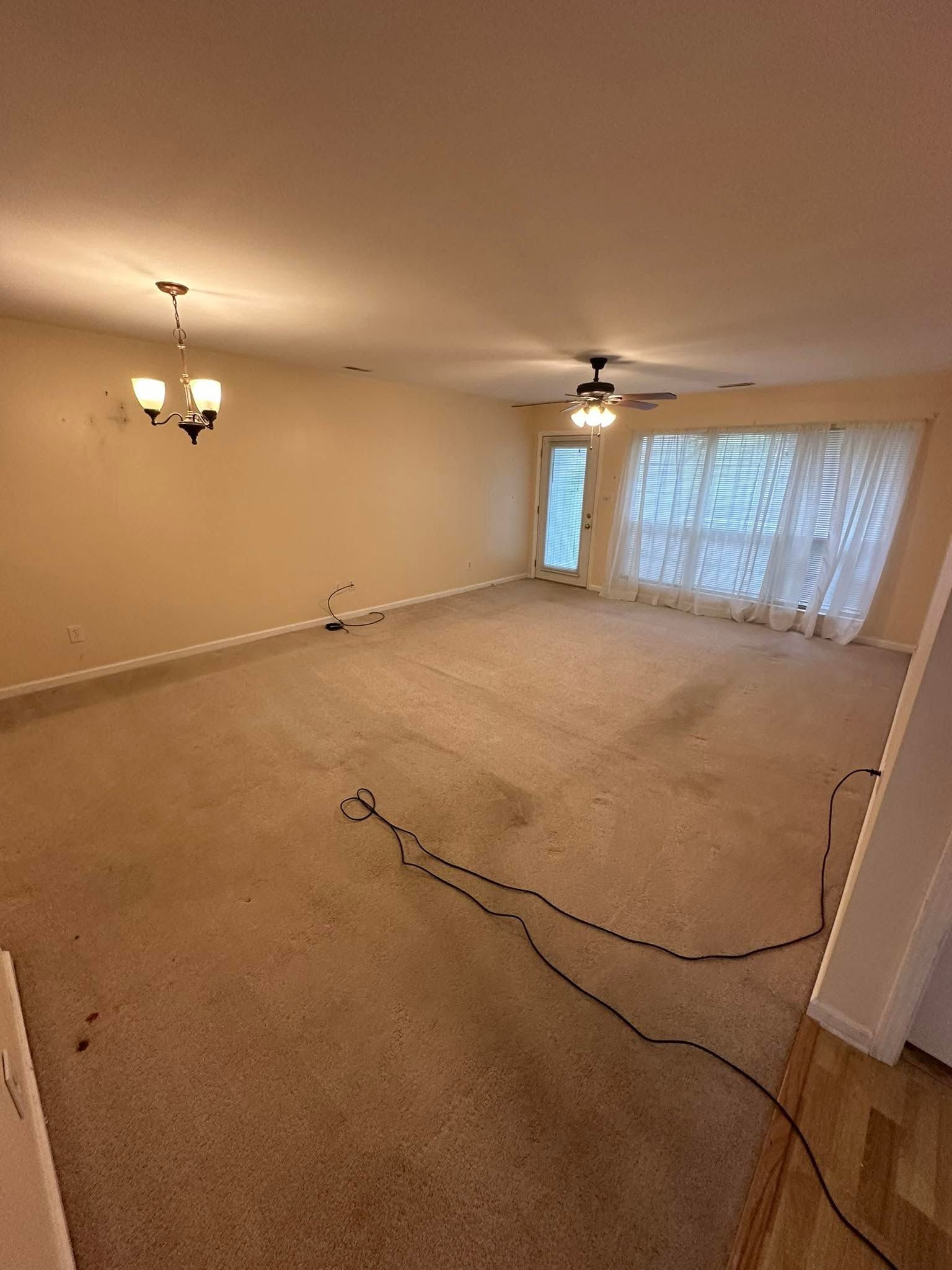 Empty carpeted living room with chandelier, ceiling fan, and large sliding glass doors.