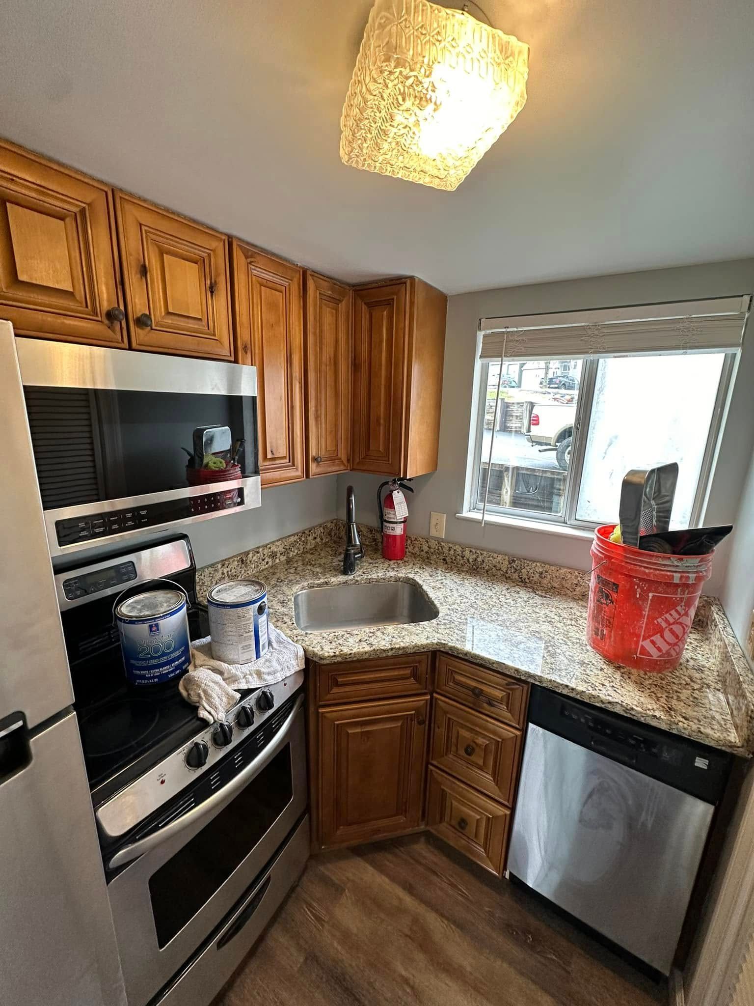 Small kitchen with wood cabinets, granite counters, stainless appliances, and a sink by a window.